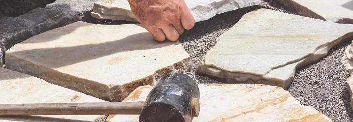 Person verlegt Steinplatten mit Gummihammer